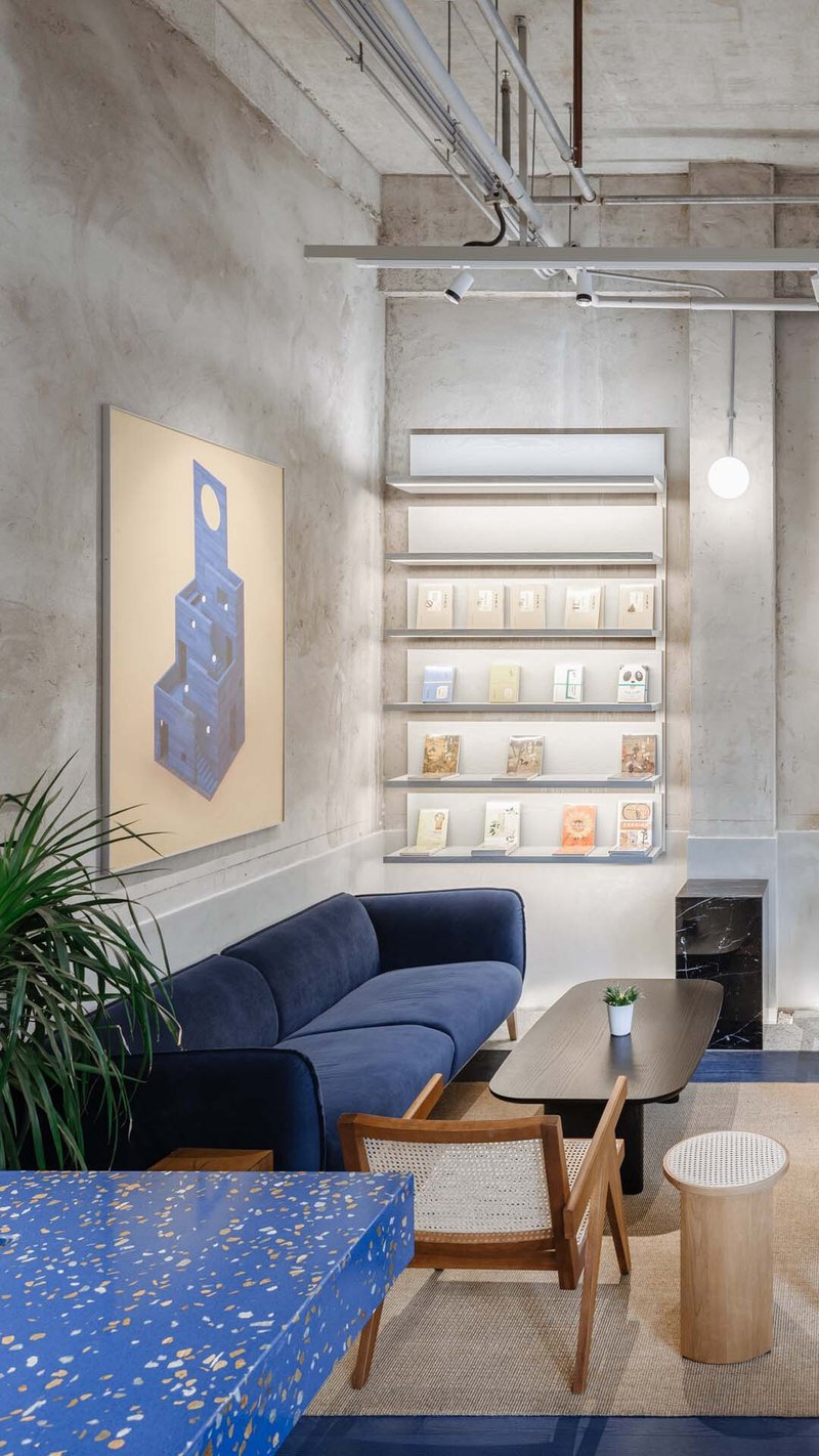 Seating area with exposed concrete walls, track lighting, and backlit display shelves near a potted plant