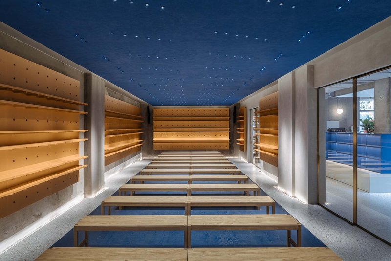 Interior retail space with timber display shelves, benches, and a perforated blue ceiling lit from above
