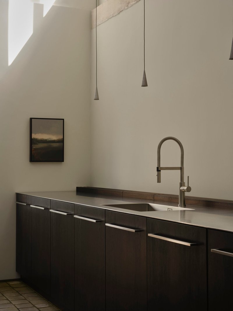 Dark timber kitchen cabinetry with stainless steel countertop and conical pendant lights above terracotta tile floor
