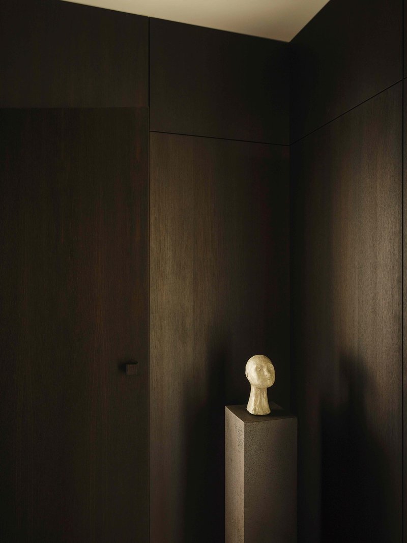 Dark timber wall panels in a corner with a sculptural bust on a pedestal illuminated by soft light