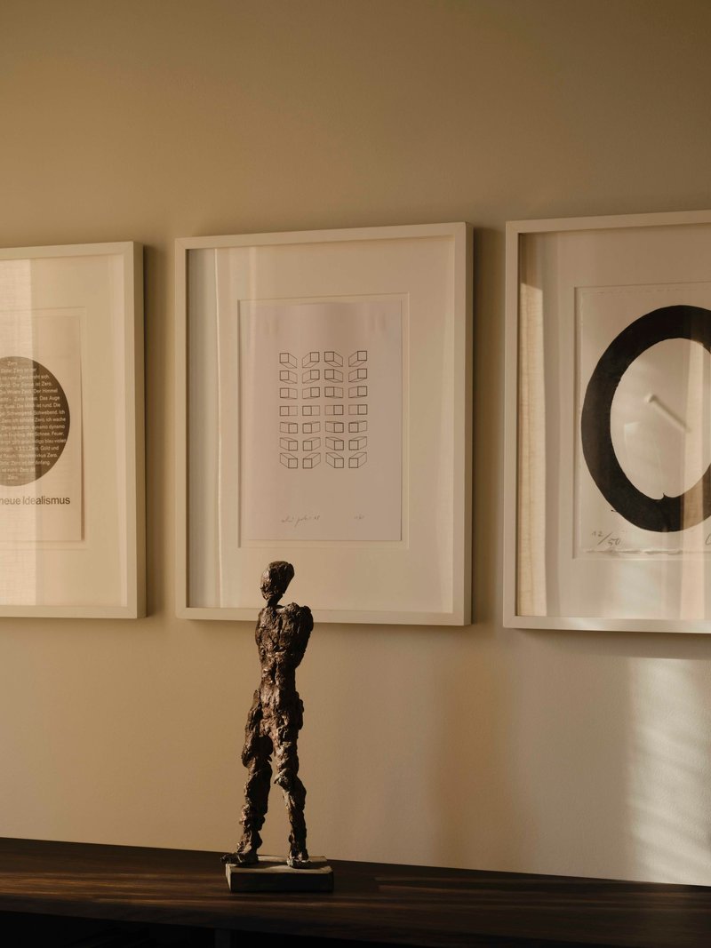 Bronze figure sculpture on a dark timber shelf beneath three framed artworks in afternoon light