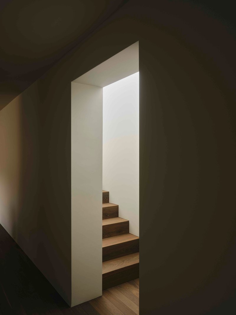 Narrow stairwell with timber treads framed by dark gray walls and natural light from above
