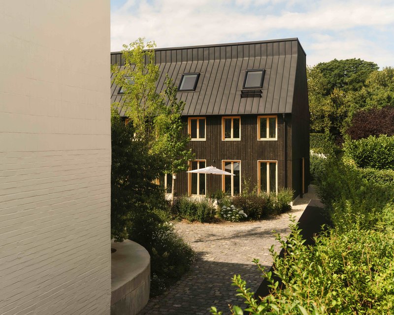Dark timber-clad facade with vertical cladding and skylights framed by courtyard plantings in summer