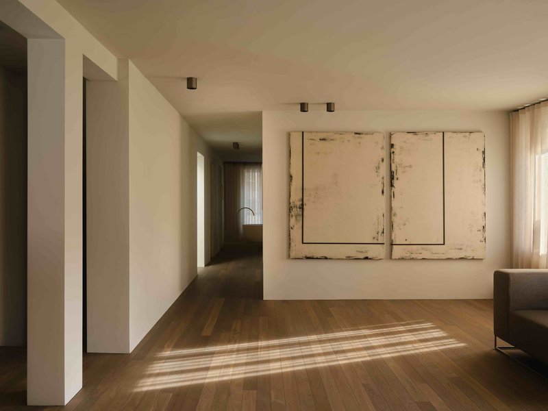 White corridor with recessed doorways and striped sunlight falling across timber floorboards
