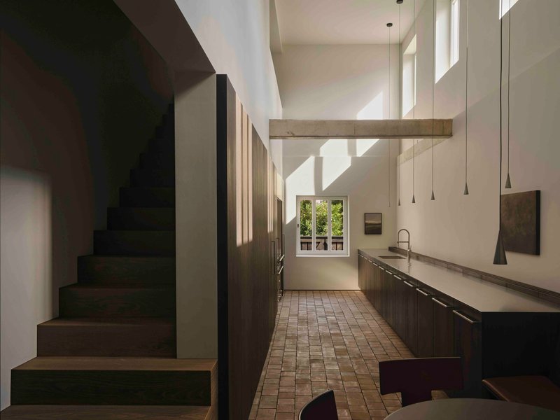 Double-height kitchen with dark timber stair and pendant lights above tiled floor