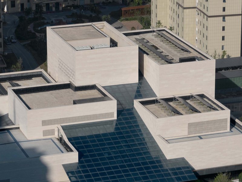 Rooftop view showing glass skylight grid connecting white concrete volumes with planted roof terraces