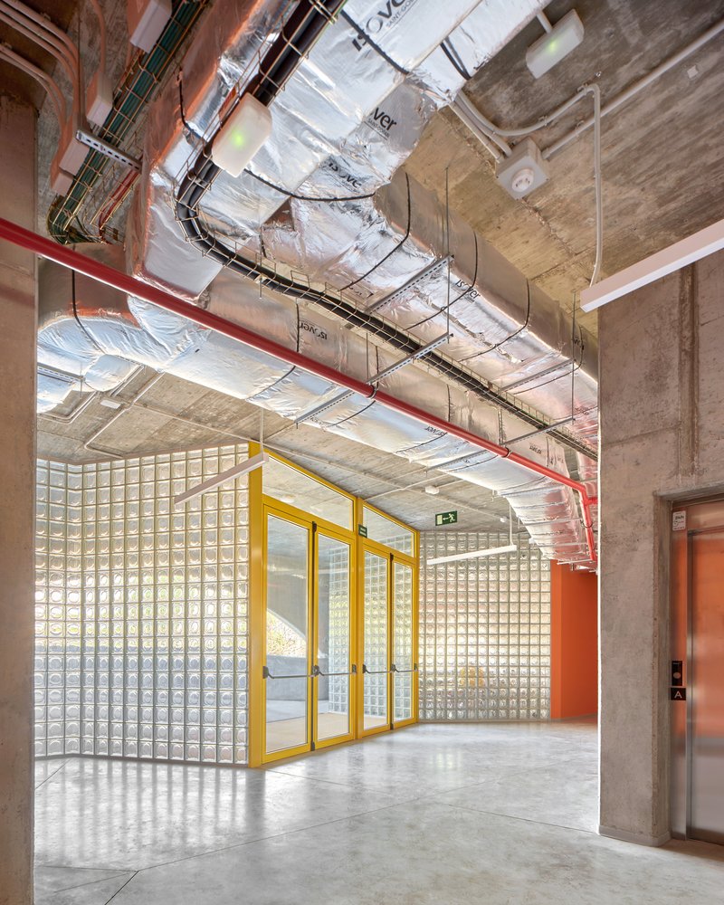 Circulation hallway with exposed ductwork and yellow-framed glass block partition wall
