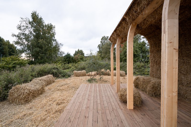 Open pavilion with timber posts and straw bale walls framing views of the surrounding landscape