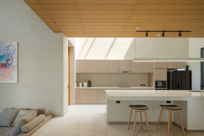 Open kitchen and living area with timber panel ceiling and two wooden stools at the island