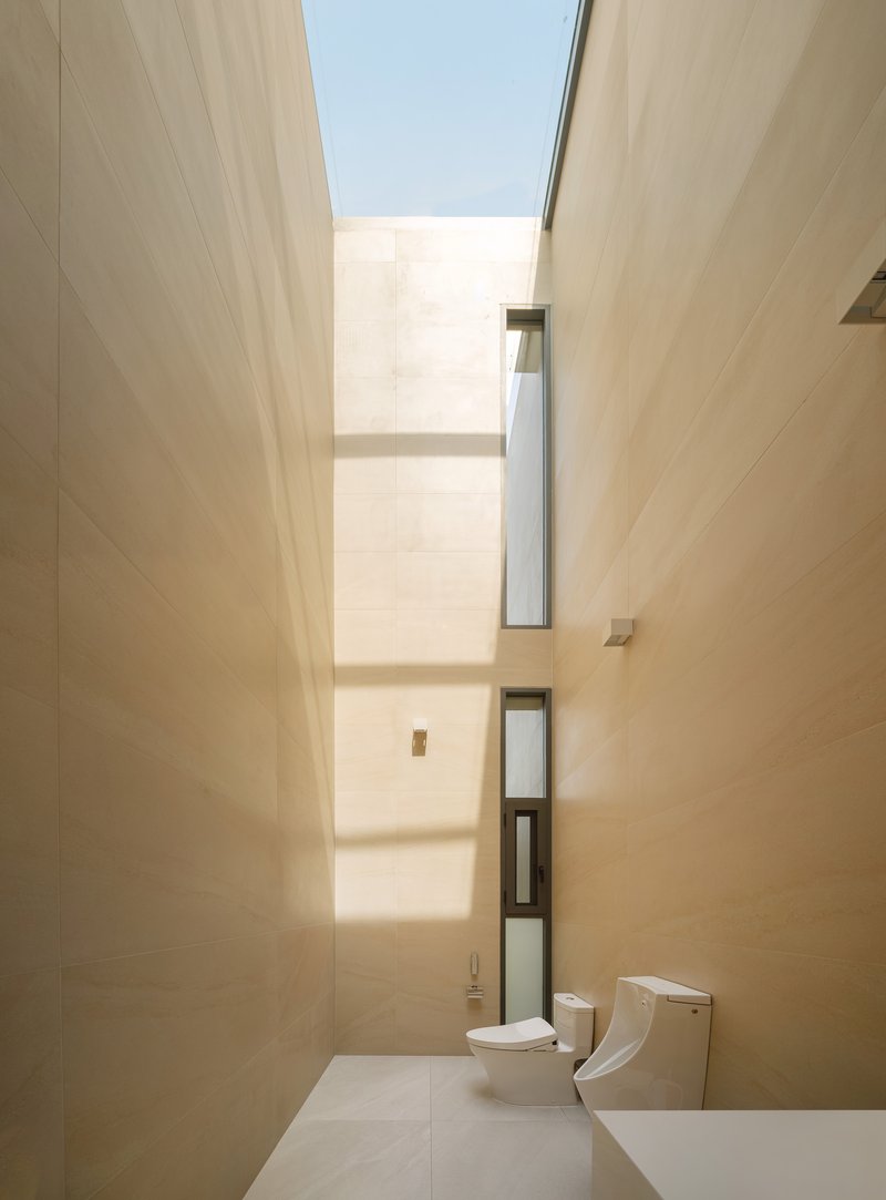 Bathroom with tall skylight shaft drawing natural light down between beige tiled walls