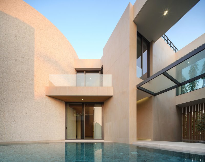 Courtyard pool at dusk with cantilevered balcony and floor-to-ceiling glazed entrance below