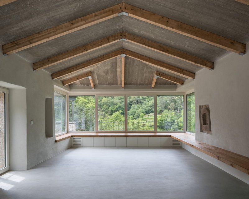 Interior room with exposed timber truss ceiling, continuous window bench and polished concrete floor facing the landscape