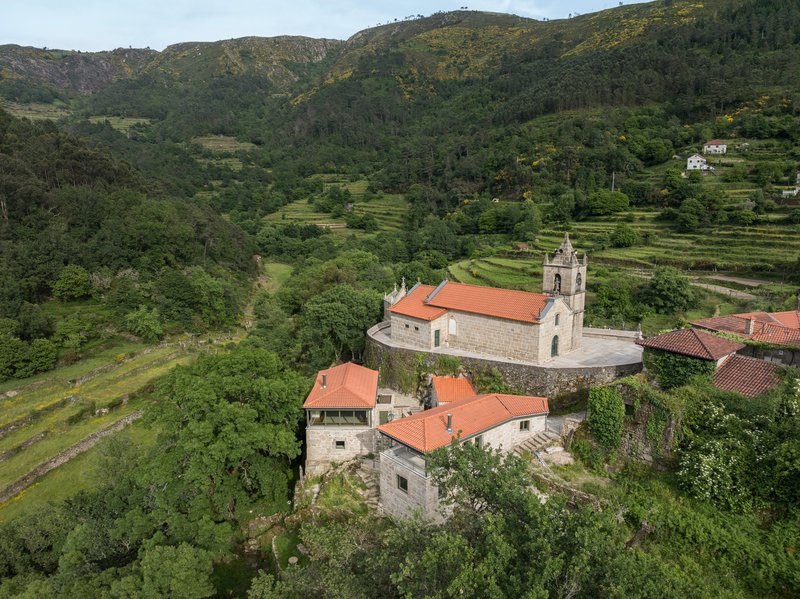 Aerial view of stone buildings with terracotta roofs nestled among terraced fields and forested hillsides