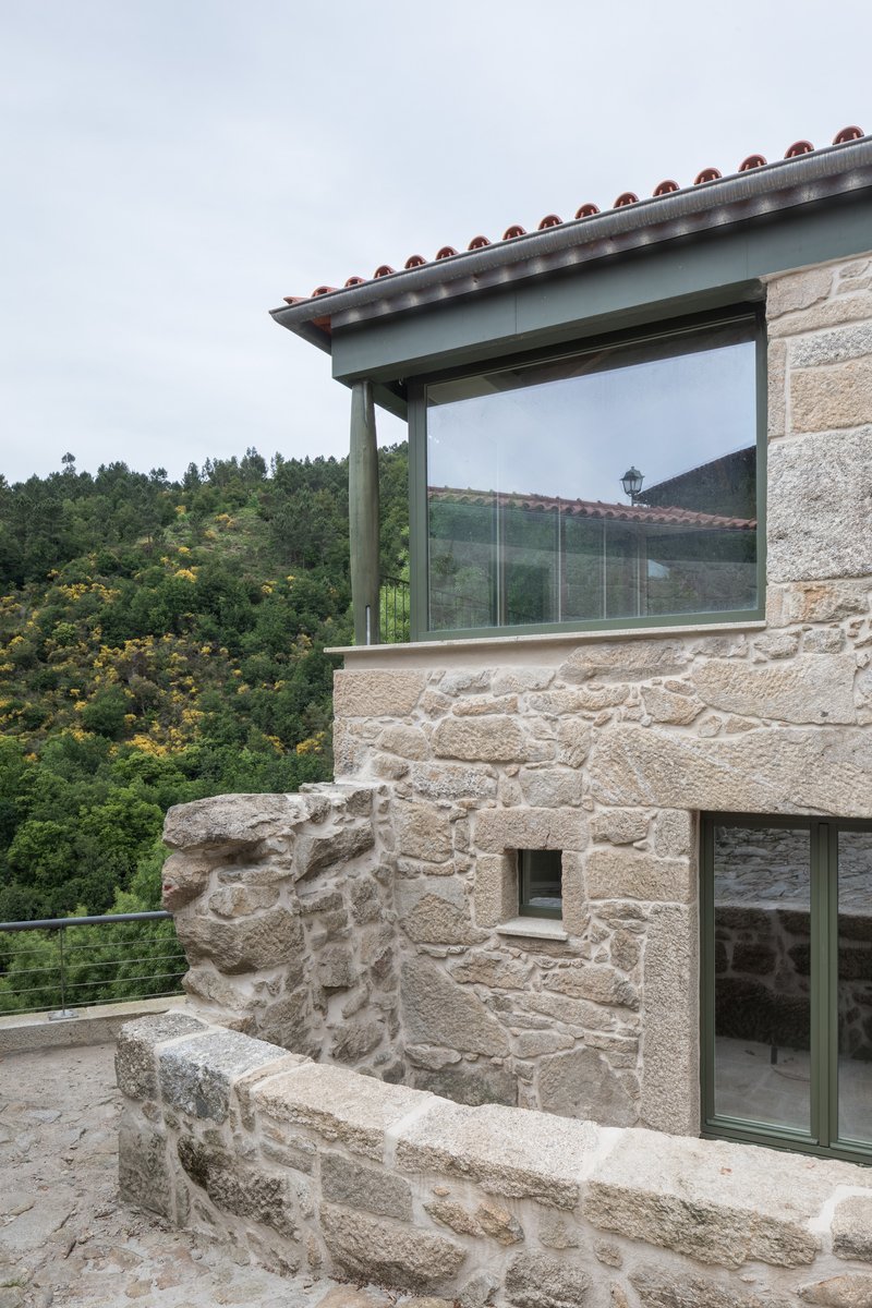 Glass-enclosed upper volume with terracotta tile eave projecting from weathered stone walls