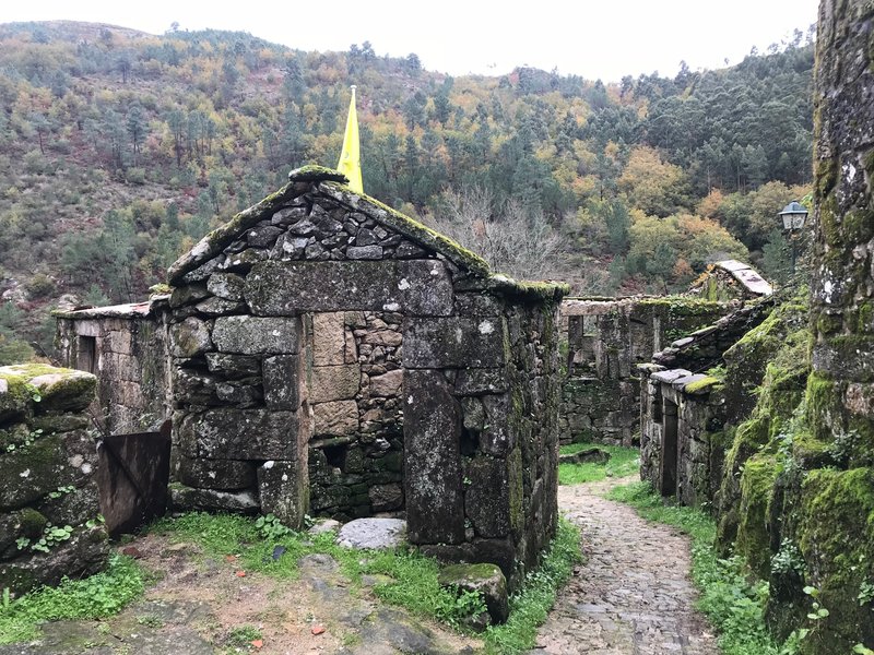 Ruins of stone structures with moss-covered walls along a cobblestone path in the hillside