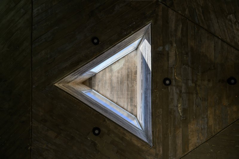Upward view of triangular skylight framed by boardform concrete ceiling with recessed lighting fixtures