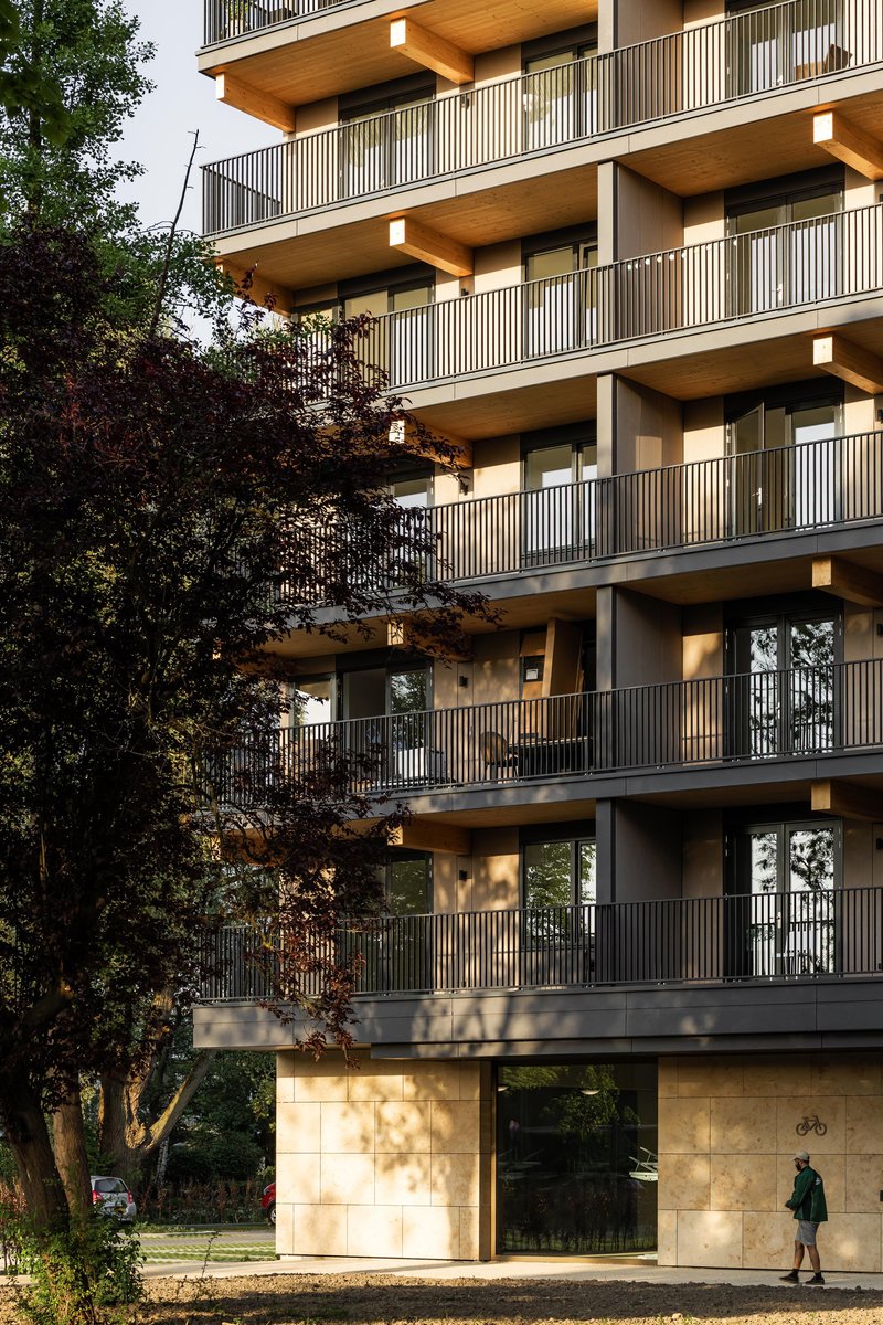 Ground floor entrance with light stone cladding framed by vertical slat balconies and foliage shadows