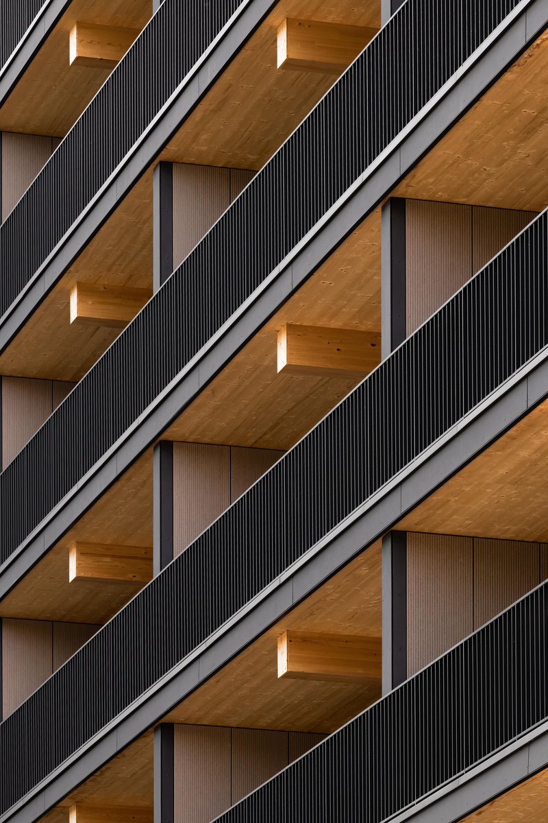 Facade detail showing diagonal balconies with dark corrugated screens and timber soffits in repeating rhythm