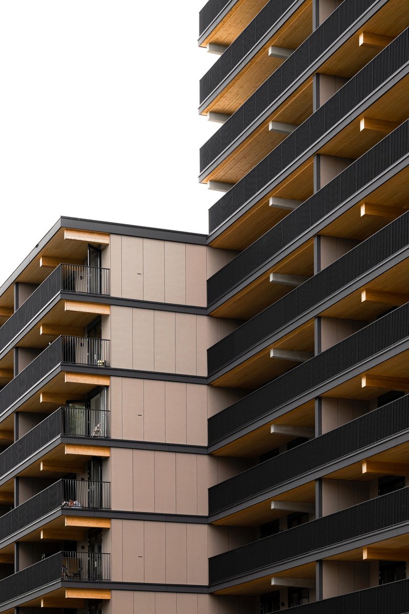 Close-up of stacked balconies with timber soffits and dark metal railings against an overcast sky