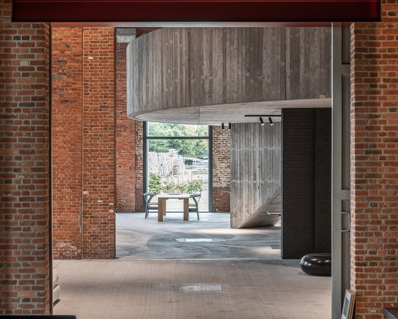 Interior view through exposed brick walls toward a cantilevered concrete volume and courtyard beyond