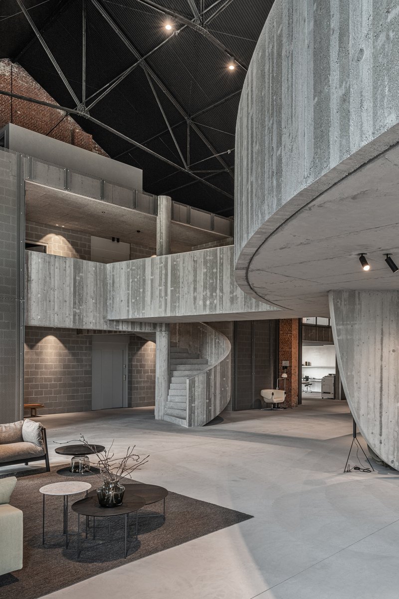 Double-height interior space with board-formed concrete stair and curved mezzanine under black metal ceiling