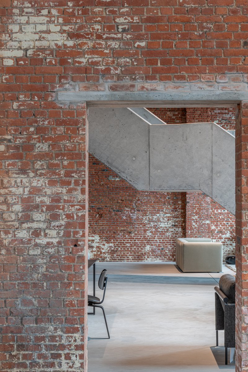 Exposed brick doorway framed by a cantilevered concrete beam above a seating area
