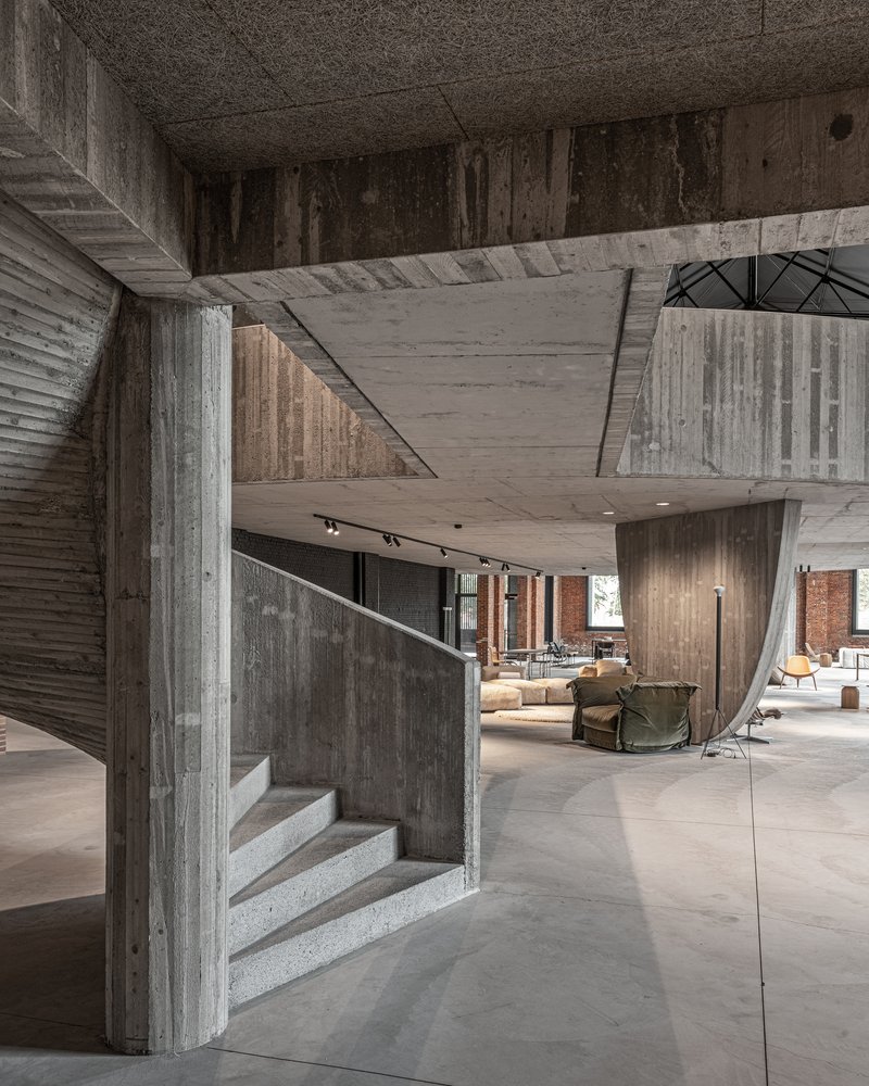 Concrete staircase wrapping around angular column beneath cantilevered upper floor slabs