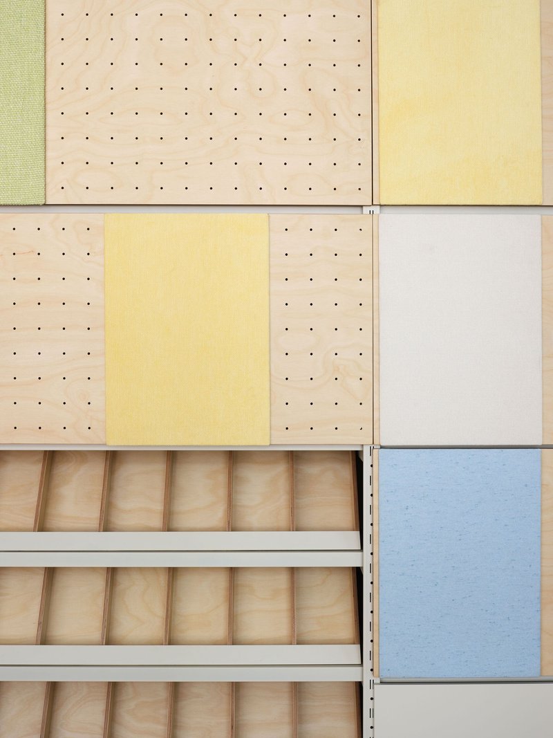 Material sample wall showing perforated plywood panels in pastel tones alongside open wooden drawer inserts