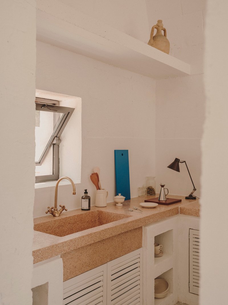 Kitchen counter with terrazzo surface, brass faucet and louvered cabinet doors below skylight