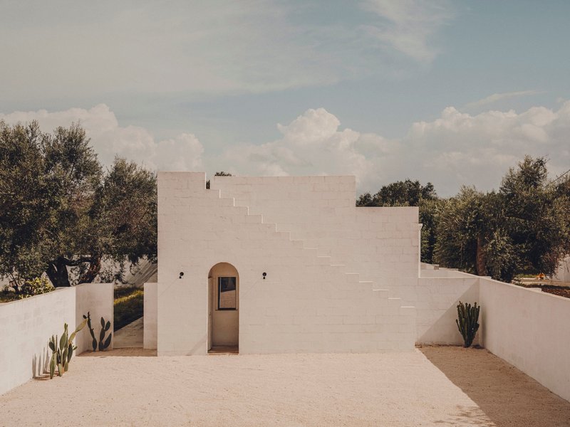 White facade with central arched doorway and stepped parapet under a cloudy sky