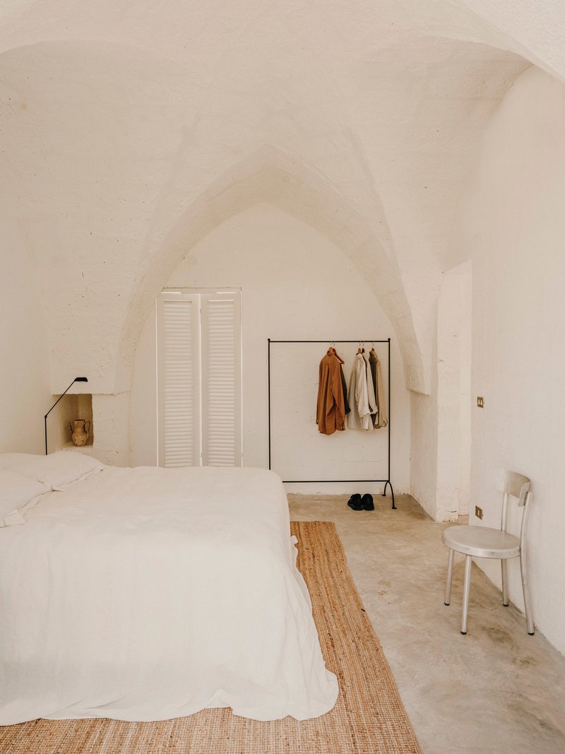 Bedroom with vaulted plaster ceiling, white louvered doors and metal clothing rack under soft daylight