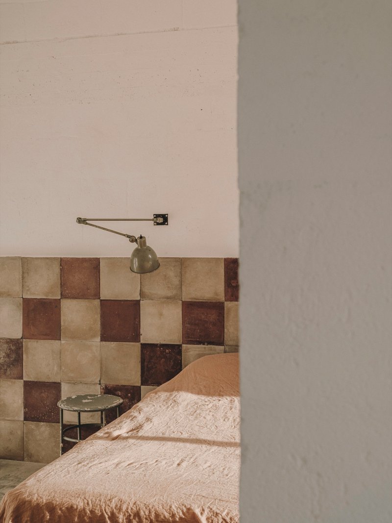 Partial view of chequered tile headboard with wall-mounted brass lamp beside plastered column
