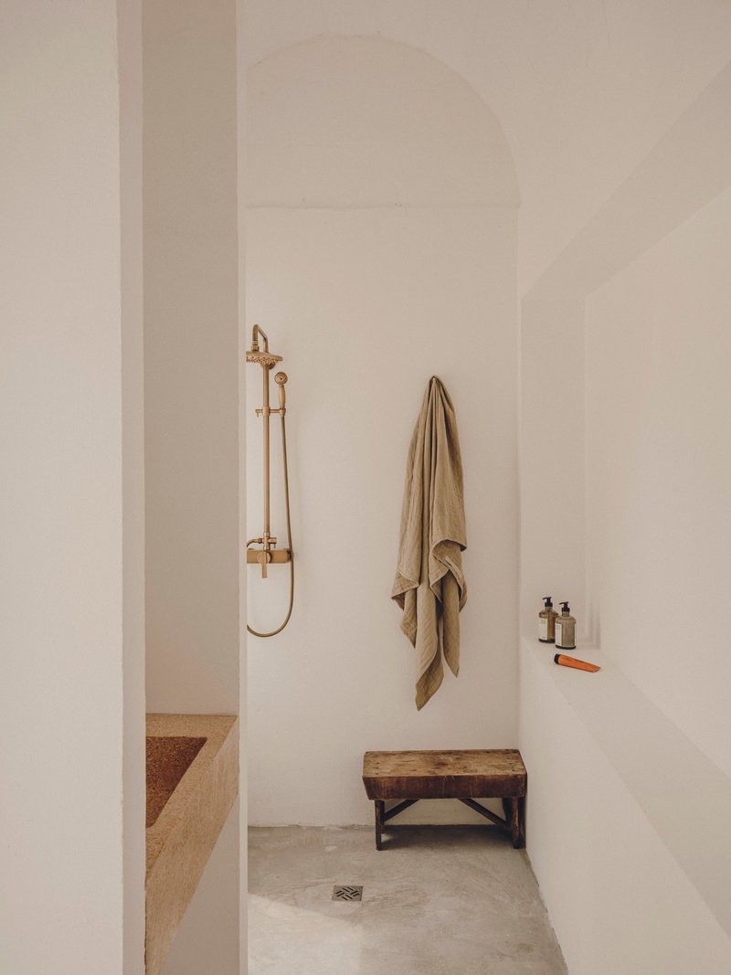 Shower alcove with brass fixtures, arched ceiling and timber bench on concrete floor