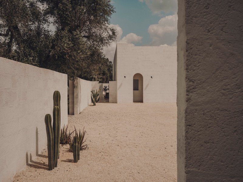 Gravel courtyard between white walls with potted cacti and arched passageway beyond