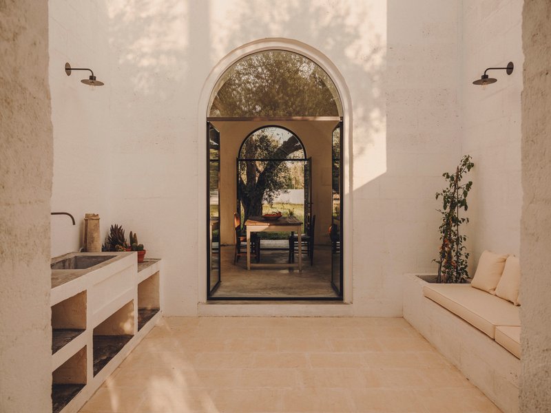 Covered terrace with built-in bench and sink looking through arched opening to dining area and tree