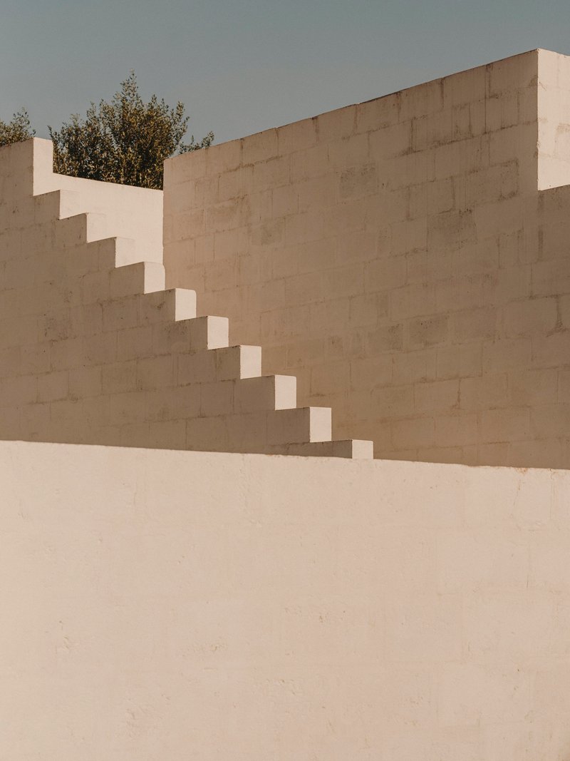 Cantilevered staircase ascending rendered wall in open courtyard beneath an overcast sky