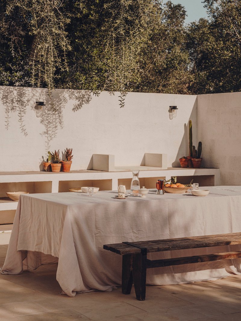 Outdoor dining table set with linen cloth beneath built-in bench seating and potted succulents