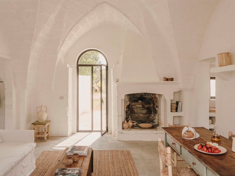Vaulted living space with arched doorway, stone fireplace surround, and timber dining table under soft daylight