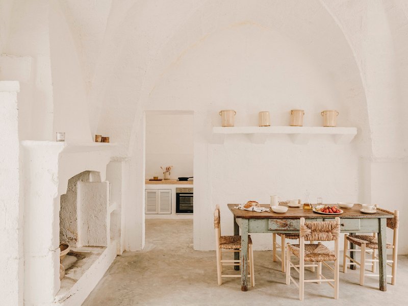 Barrel-vaulted dining room with rustic table, woven rush chairs, and a stepped fireplace niche