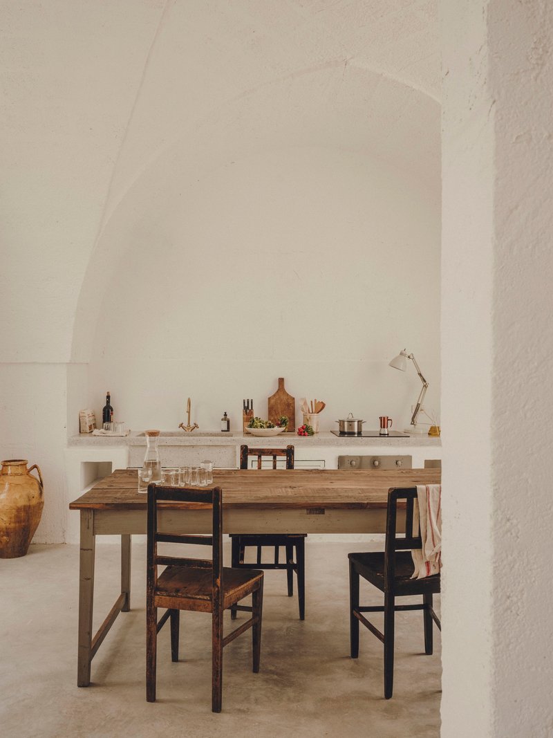 Dining area with timber table and mismatched chairs beneath a vaulted white plaster ceiling