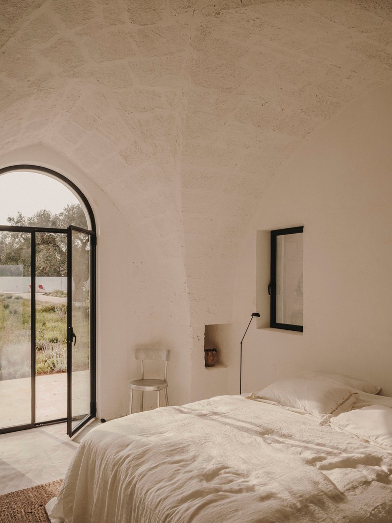 Bedroom with arched steel-framed glass door opening to garden with olive trees beyond