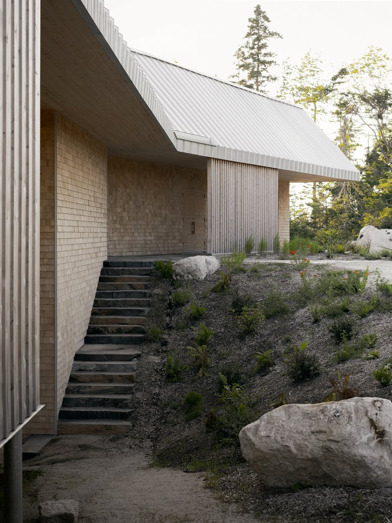 Exterior steel staircase ascending planted slope between cream brick wall and corrugated metal cladding