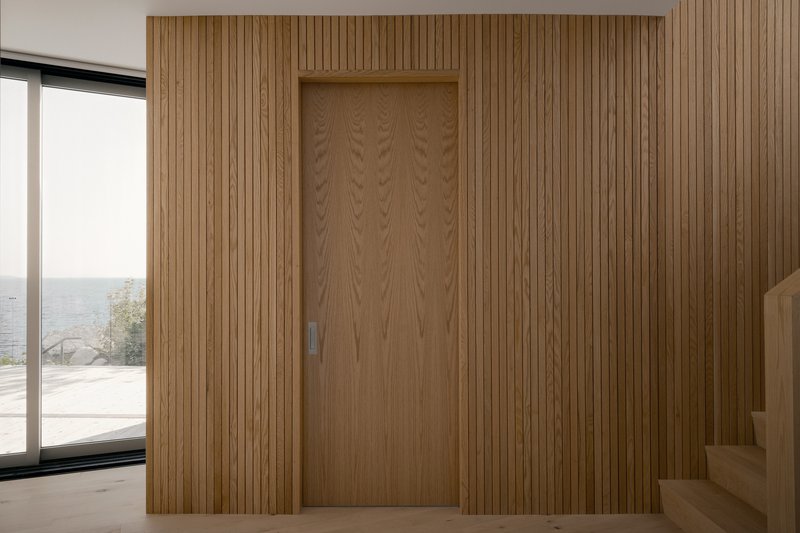 Vertical timber slat wall concealing recessed door with view to terrace and sea beyond