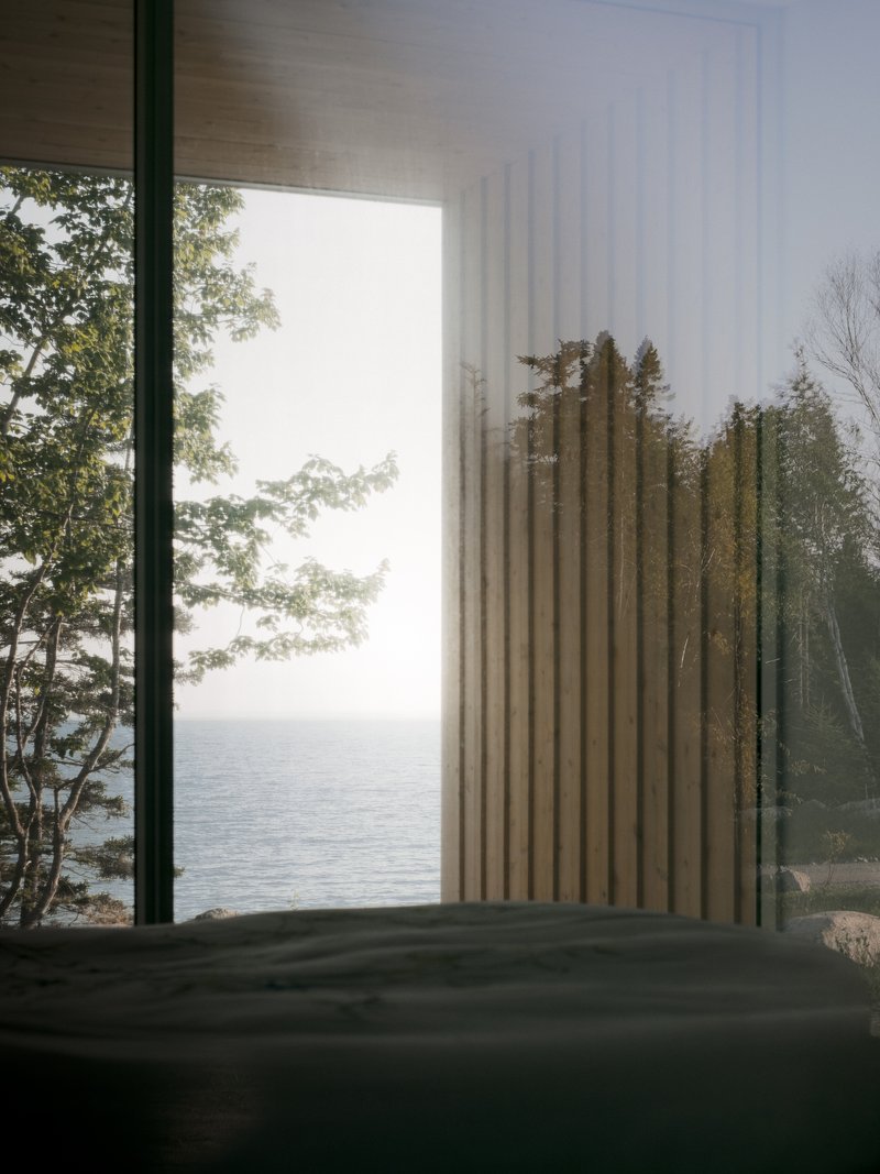 Interior view through vertical timber slats framing trees and lake water beyond