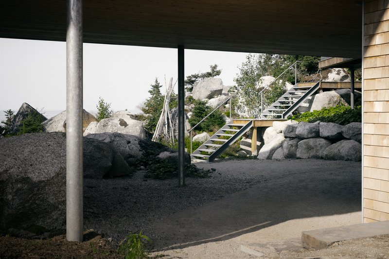 Covered outdoor space with steel column, exterior staircase and boulders under overcast sky