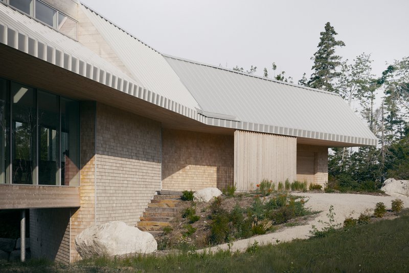 Exterior facade combining pale brick, vertical wood cladding, and a sweeping metal roof