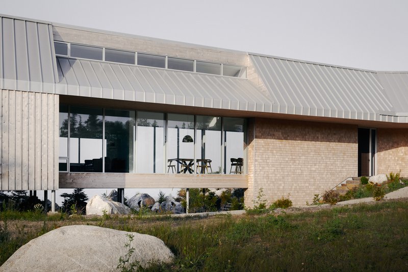 Elevated glazed living area with standing seam metal roof above a cream brick plinth in dry grasses