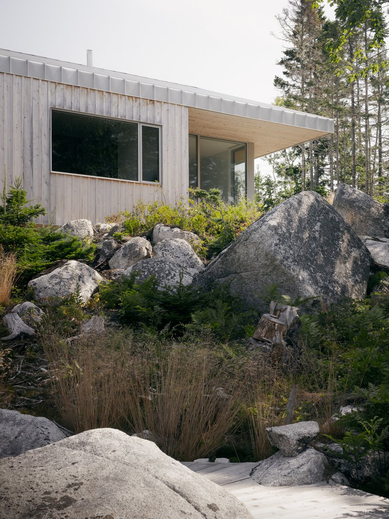 Timber-clad volume with metal seam roof nestled among granite outcrops and low plantings