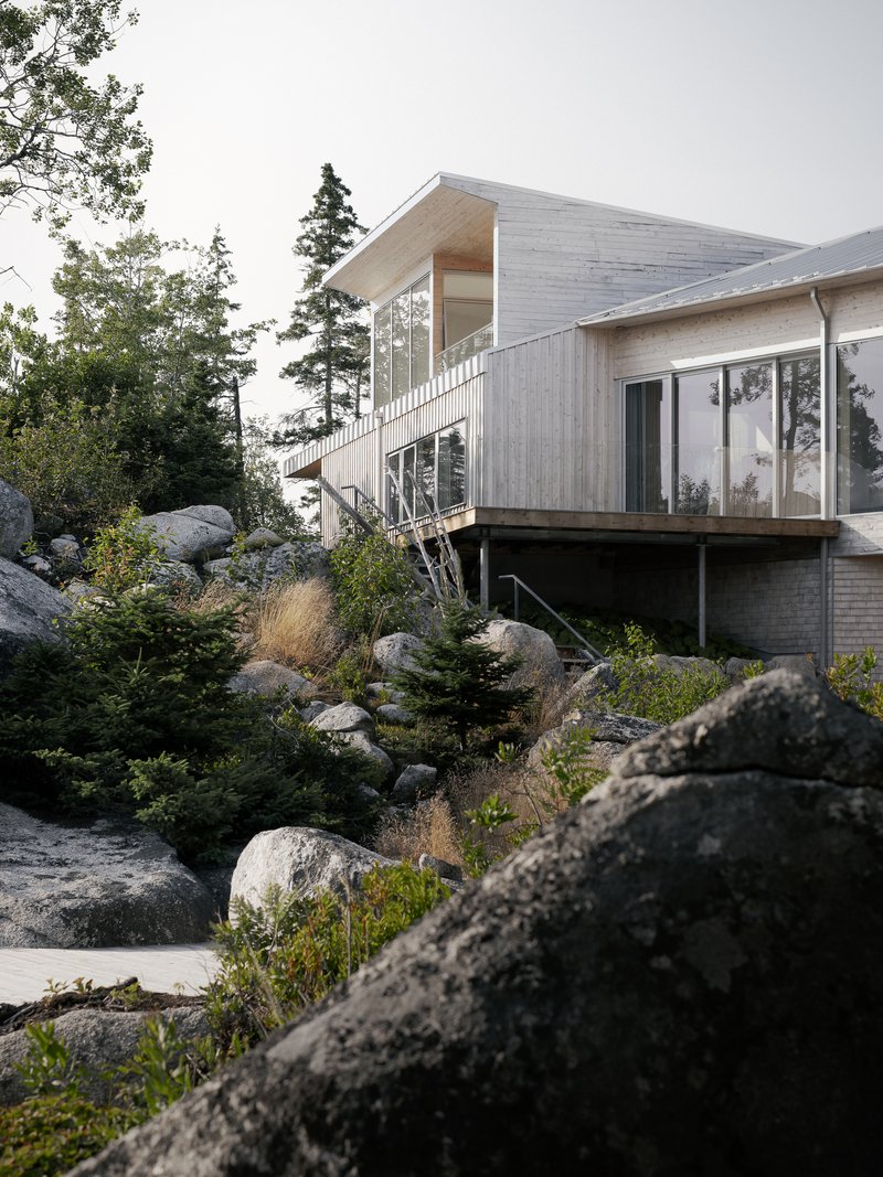 Two-story glazed corner stairwell connecting timber volumes above a rocky planted slope