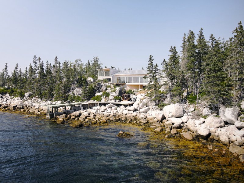 Waterfront house on a rocky outcrop with evergreen forest and small dock extending into calm water